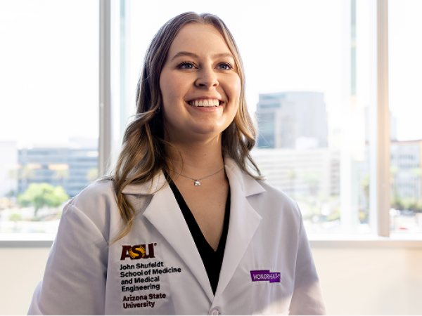 A doctor in a white coat stands in front of a window and smiles